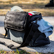 Back of a Local Discs disc golf bag with discs and rag on a tee pad